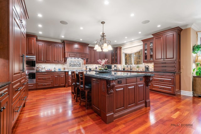 kitchen with a kitchen bar, pendant lighting, dark stone countertops, hardwood / wood-style floors, and a center island