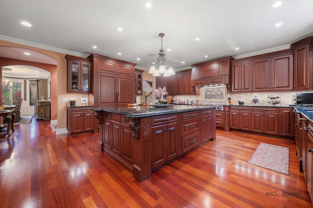 kitchen with hanging light fixtures, a notable chandelier, backsplash, dark stone countertops, and an island with sink