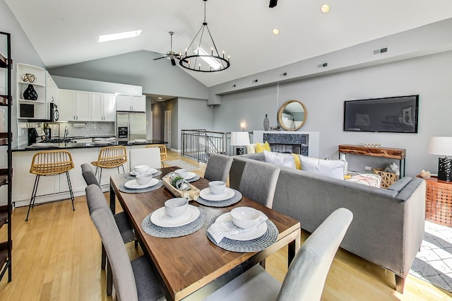 dining room featuring a premium fireplace, a chandelier, light hardwood / wood-style floors, and lofted ceiling with skylight