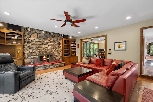 living room with a stone fireplace, hardwood / wood-style floors, and ceiling fan