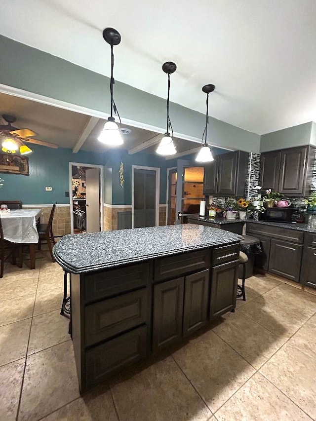 kitchen featuring beam ceiling, hanging light fixtures, dark brown cabinets, ceiling fan, and a kitchen island