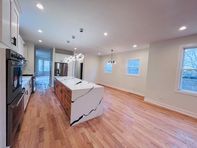 kitchen with pendant lighting, light hardwood / wood-style flooring, light stone countertops, a large island, and white cabinetry