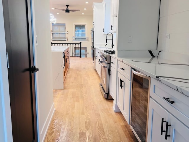 kitchen with white cabinetry, stainless steel range, ceiling fan, sink, and wine cooler