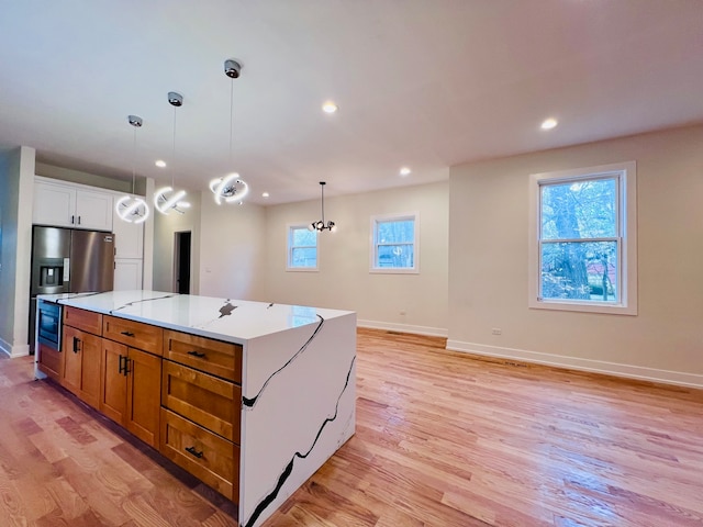 kitchen with light stone countertops, a center island, light hardwood / wood-style floors, white cabinetry, and hanging light fixtures