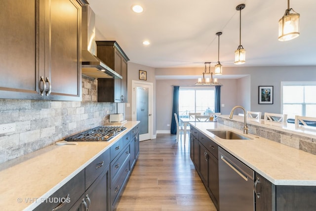 kitchen with appliances with stainless steel finishes, sink, wall chimney range hood, and decorative light fixtures