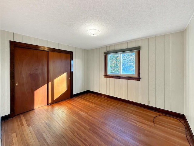 103 E Roosevelt St, Freeport, IL 61032 - unfurnished bedroom with hardwood / wood-style floors, a textured ceiling, baseboards, wooden walls, and a closet