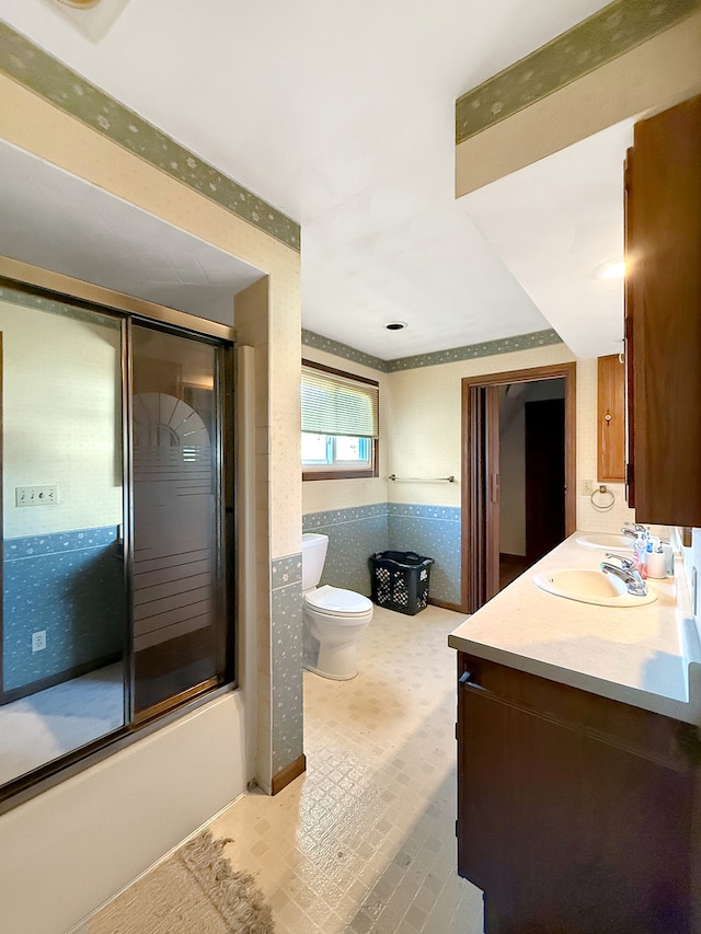 full bathroom featuring tile walls, bath / shower combo with glass door, vanity, and toilet