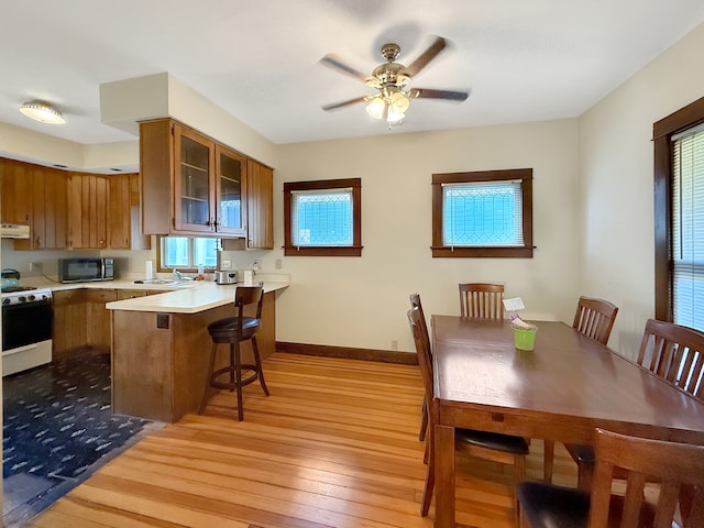 kitchen with white gas range, a breakfast bar, kitchen peninsula, ceiling fan, and light wood-type flooring