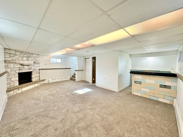 basement with a paneled ceiling, a stone fireplace, carpet floors, and baseboard heating