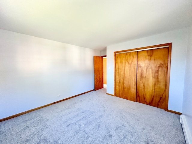 unfurnished bedroom featuring a closet, a baseboard heating unit, and light colored carpet