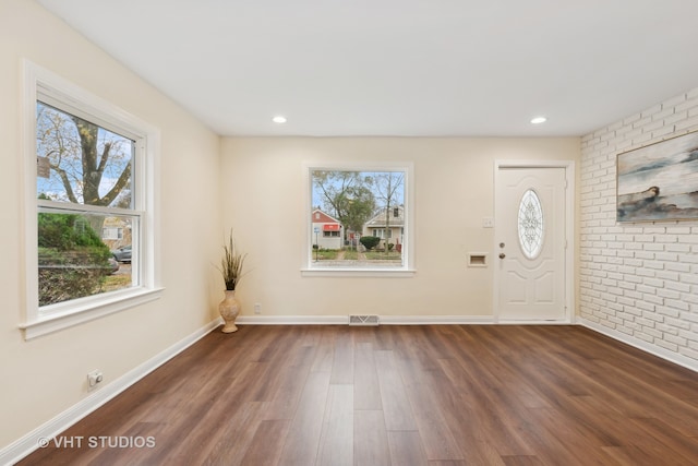 foyer entrance featuring a wealth of natural light, dark hardwood / wood-style flooring, and brick wall