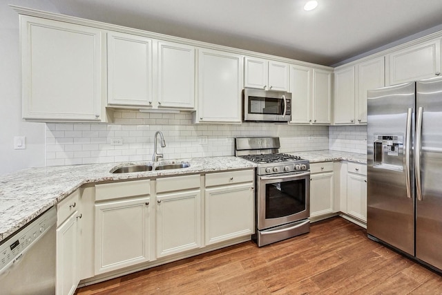 kitchen with sink, light stone countertops, light wood-type flooring, tasteful backsplash, and stainless steel appliances