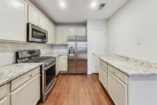 kitchen with tasteful backsplash, light stone counters, hardwood / wood-style floors, white cabinets, and appliances with stainless steel finishes