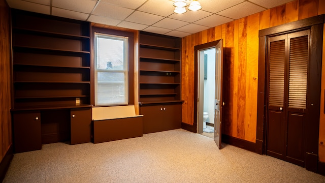 unfurnished office featuring a paneled ceiling, light carpet, and wooden walls