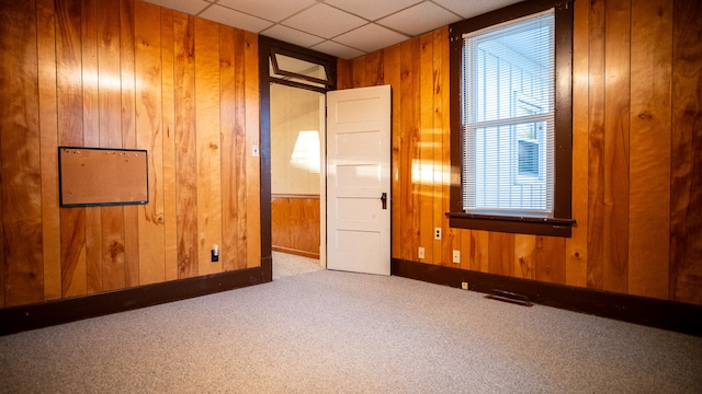 carpeted empty room with a paneled ceiling and wood walls