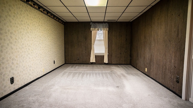 carpeted empty room with a drop ceiling and wood walls