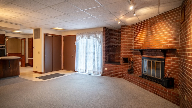 unfurnished living room featuring light carpet, brick wall, a brick fireplace, rail lighting, and a paneled ceiling