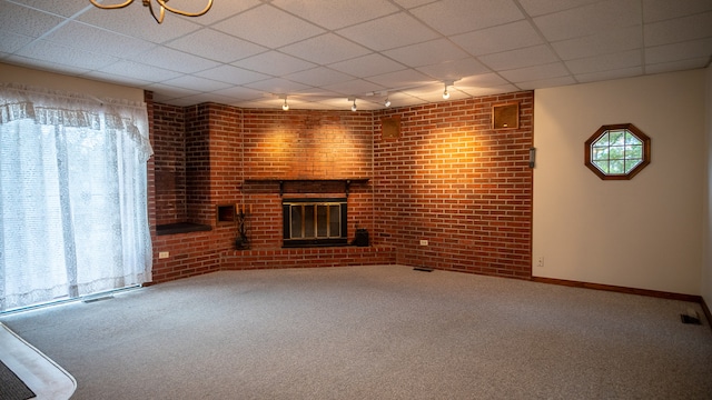 unfurnished living room featuring track lighting, carpet, a paneled ceiling, a fireplace, and brick wall