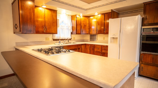 kitchen featuring oven, kitchen peninsula, white refrigerator with ice dispenser, and stainless steel gas cooktop