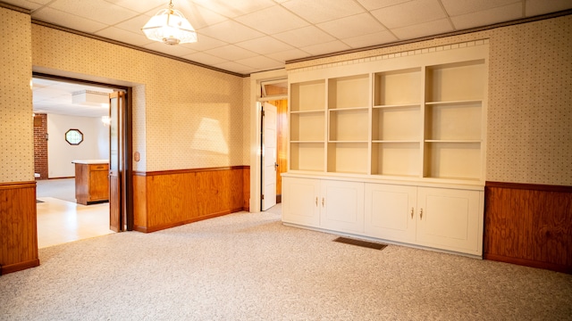 empty room featuring a drop ceiling, built in shelves, and wood walls