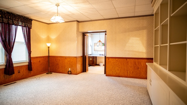 carpeted empty room with ornamental molding, a paneled ceiling, and wood walls