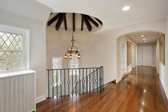 corridor with a wealth of natural light, dark wood-type flooring, a notable chandelier, and radiator