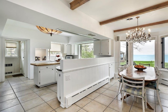 kitchen featuring white cabinetry, a water view, beam ceiling, decorative light fixtures, and a baseboard heating unit