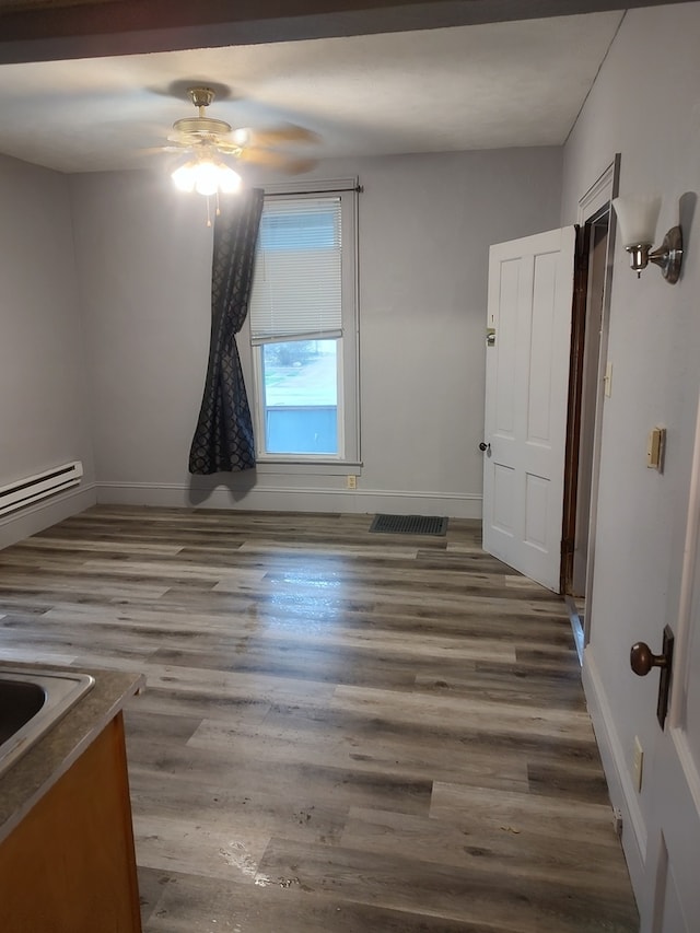 spare room with ceiling fan, wood-type flooring, and a baseboard heating unit