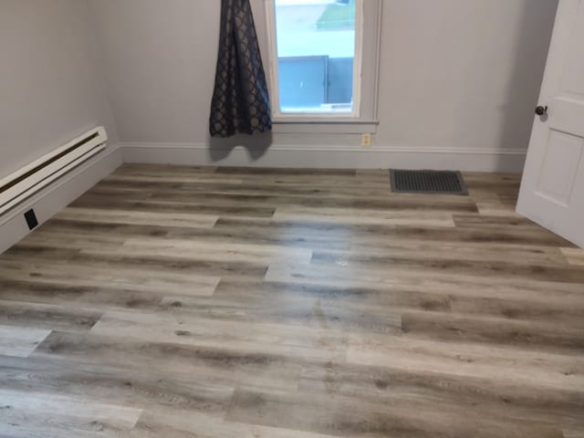 empty room with hardwood / wood-style floors and a baseboard radiator