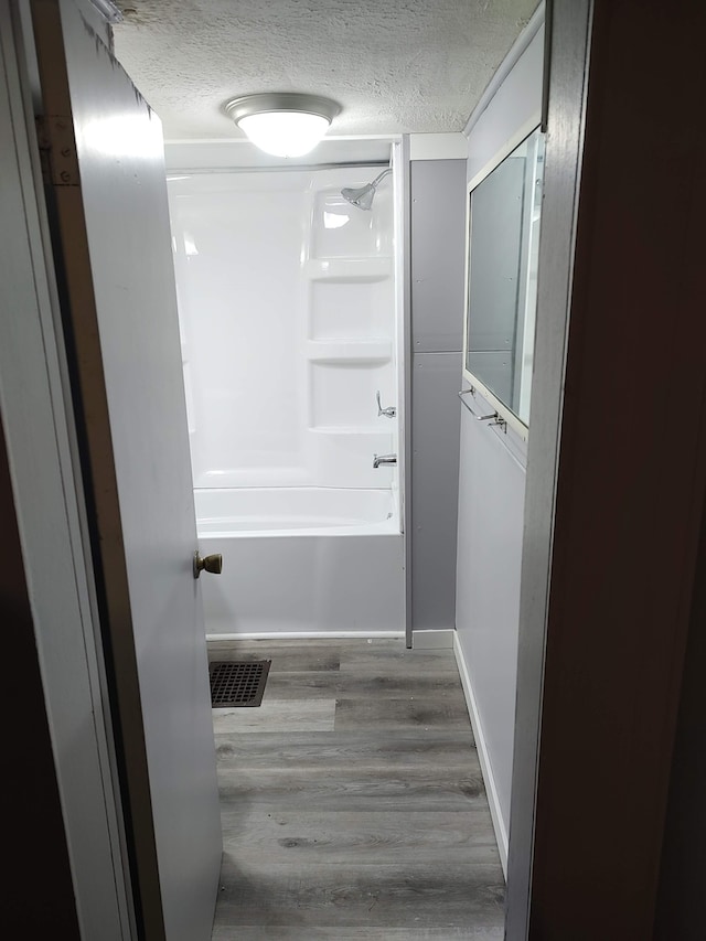 bathroom featuring a textured ceiling, bathing tub / shower combination, and hardwood / wood-style flooring