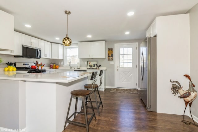 kitchen with sink, kitchen peninsula, appliances with stainless steel finishes, white cabinets, and dark wood-type flooring