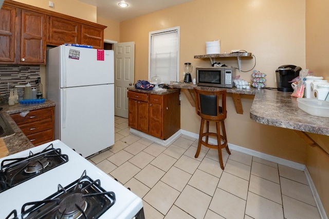 kitchen featuring white appliances, tasteful backsplash, light tile patterned floors, and a kitchen breakfast bar