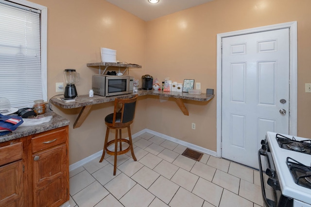 kitchen featuring a kitchen breakfast bar, kitchen peninsula, white gas stove, and light tile patterned floors