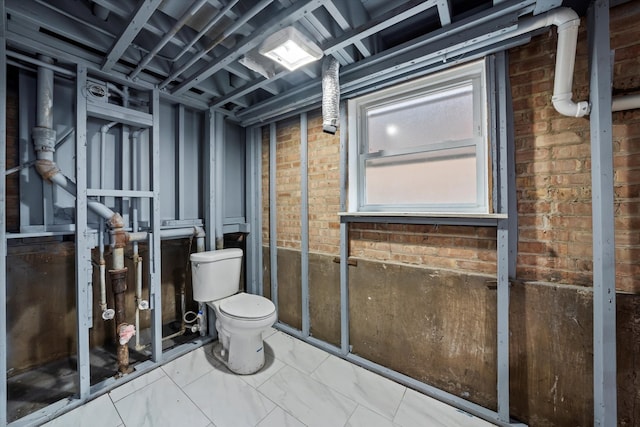 bathroom featuring brick wall and toilet