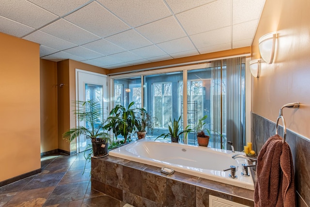 full bathroom with a drop ceiling, baseboards, a garden tub, and stone tile flooring