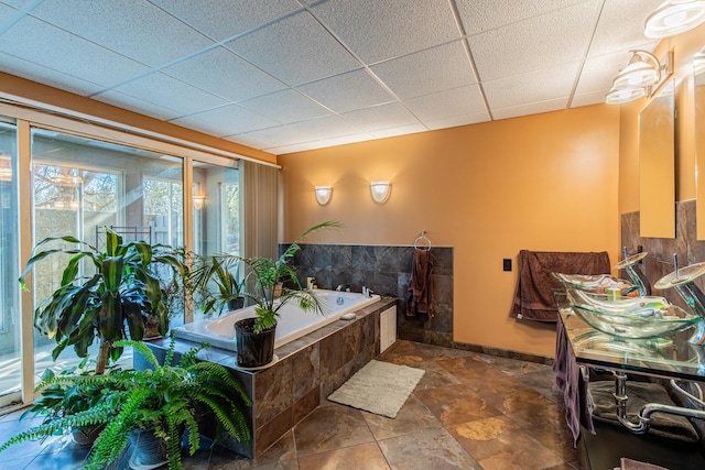 bathroom with stone finish flooring, baseboards, a drop ceiling, a garden tub, and vanity