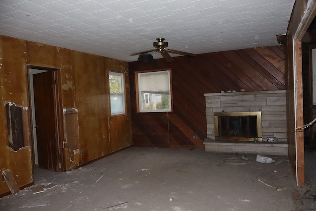 unfurnished living room featuring a stone fireplace, wooden walls, and ceiling fan