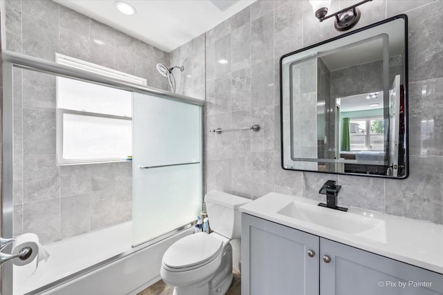 bathroom with toilet, backsplash, tile walls, bath / shower combo with glass door, and vanity