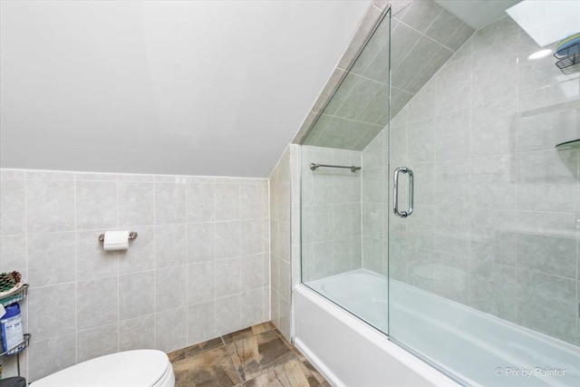 full bathroom featuring tile walls, toilet, combined bath / shower with glass door, and vaulted ceiling