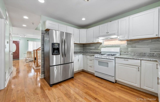 kitchen with under cabinet range hood, stainless steel fridge, white cabinetry, and gas range gas stove