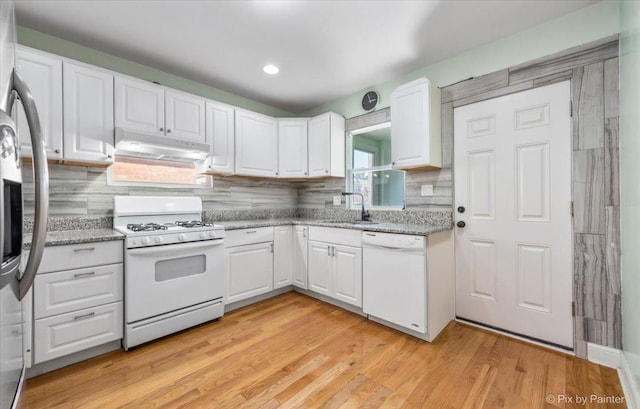 kitchen featuring white appliances, light wood-style flooring, a sink, under cabinet range hood, and white cabinetry