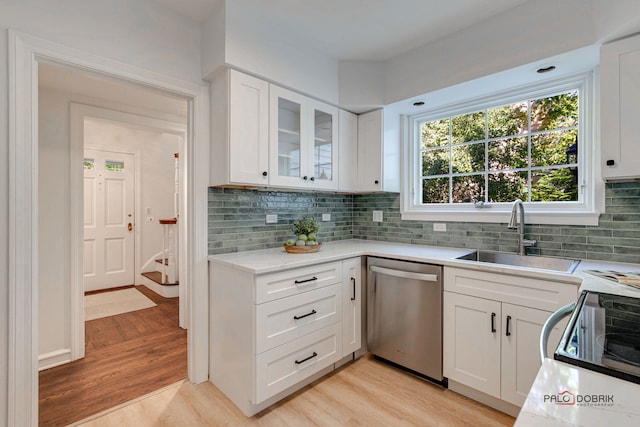 kitchen featuring sink, stainless steel dishwasher, backsplash, light hardwood / wood-style floors, and white cabinets