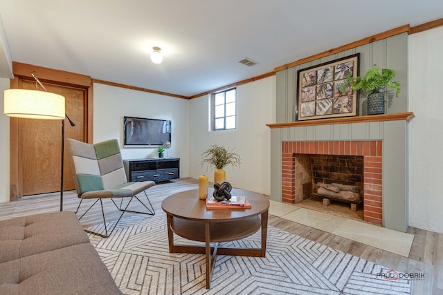 living room featuring a brick fireplace, light hardwood / wood-style flooring, and crown molding