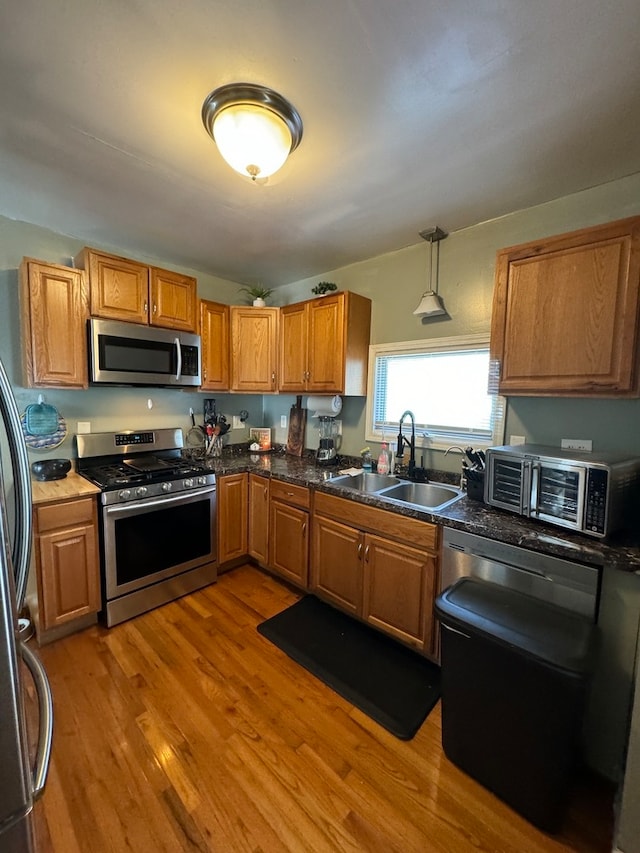 kitchen featuring sink, appliances with stainless steel finishes, light hardwood / wood-style flooring, and pendant lighting