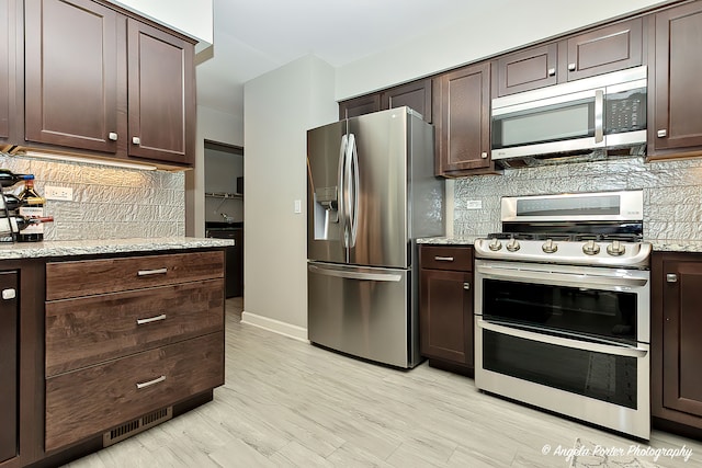 kitchen with tasteful backsplash, stainless steel appliances, dark brown cabinets, light stone countertops, and light hardwood / wood-style flooring