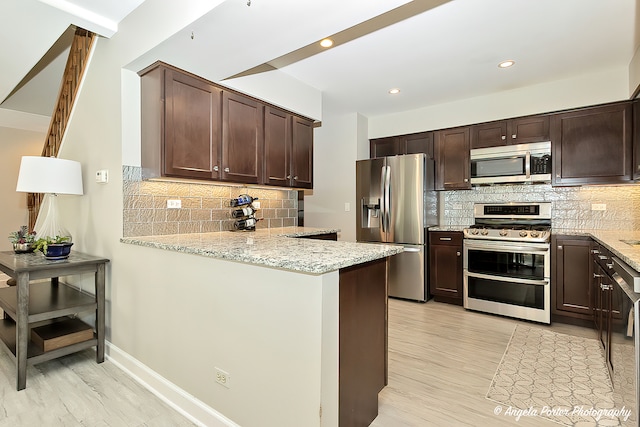 kitchen featuring kitchen peninsula, appliances with stainless steel finishes, decorative backsplash, and light stone counters