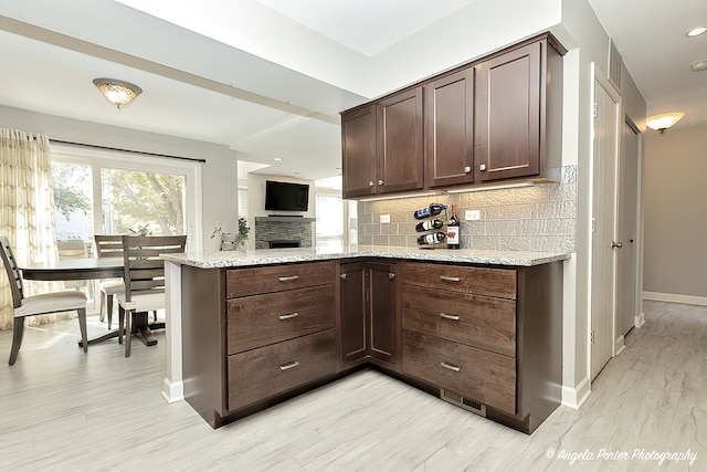 kitchen with light wood-type flooring, dark brown cabinets, and light stone counters