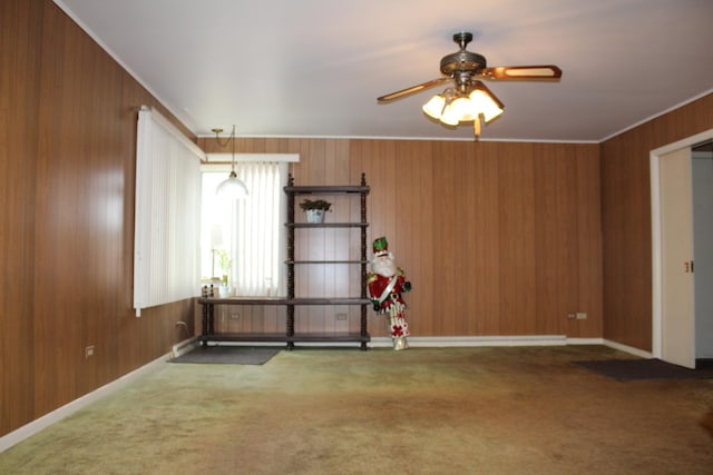 empty room with carpet floors, crown molding, ceiling fan, and wooden walls