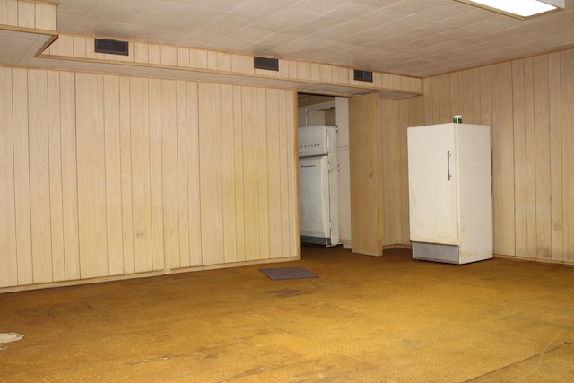 basement with carpet flooring, white fridge, and wood walls