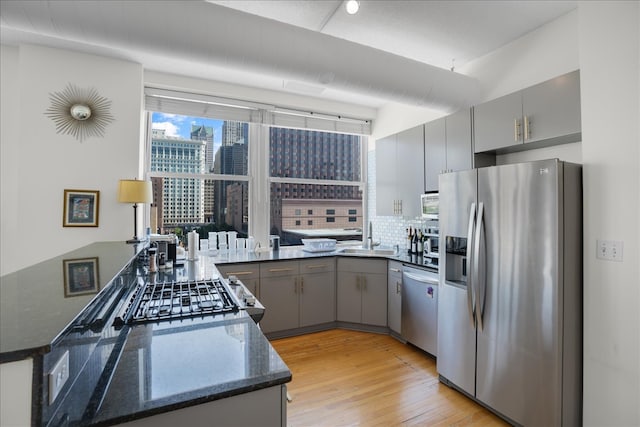 kitchen featuring kitchen peninsula, appliances with stainless steel finishes, light hardwood / wood-style flooring, dark stone countertops, and gray cabinets